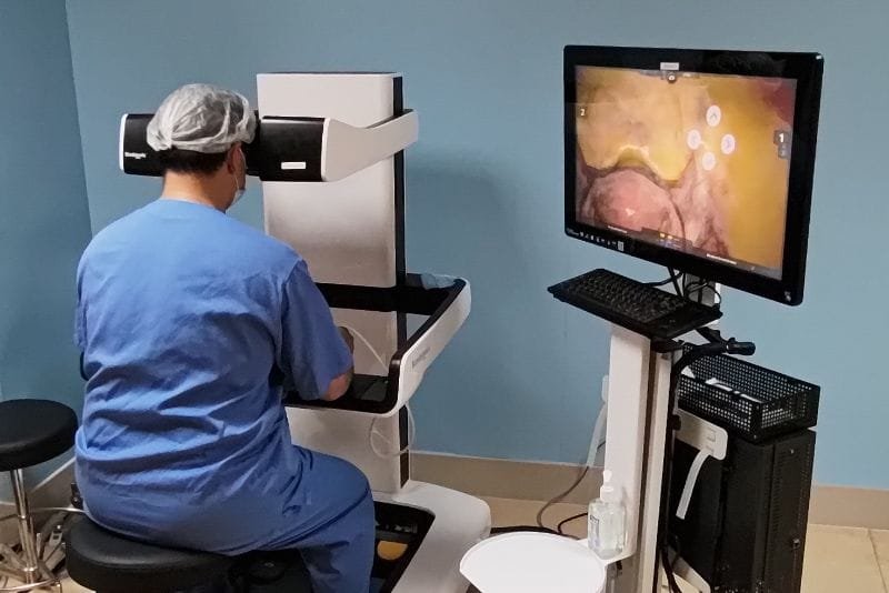 Cirurgião no console da plataforma de cirurgia robótica, visto de costas.