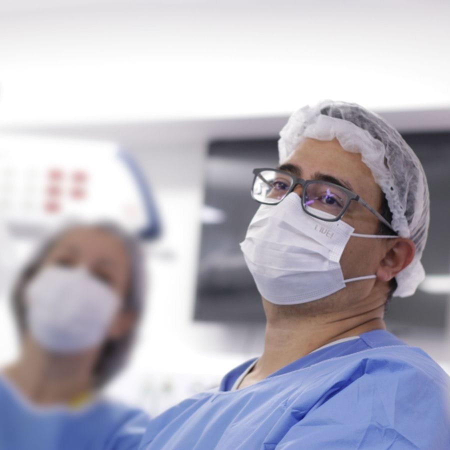 Dr. Luiz Takano no bloco cirúrgico, de máscara e óculos.