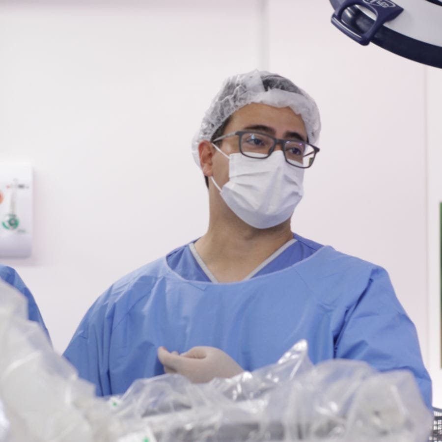 Dr. Luiz Takano no centro cirúrgico, de avental, touca, máscara e óculos.